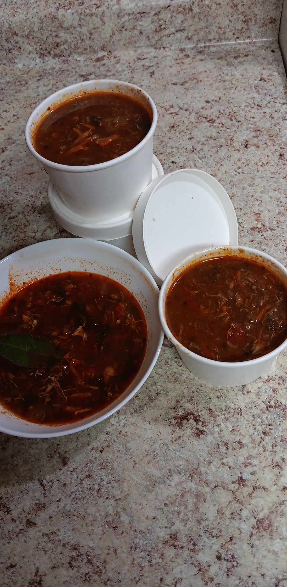 Three white plastic bowls filled with a reddish-brown stew or curry, arranged on a speckled beige countertop. Prepared by Sun Connect Foods & Services LLC, Keansburg, New Jersey.